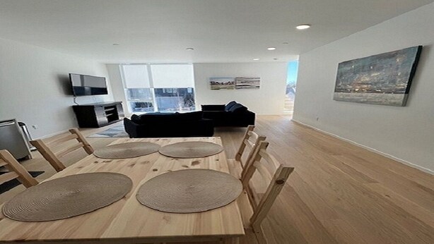 A modern living room with a wooden dining table, four chairs, a black sofa, and a television on a stand.