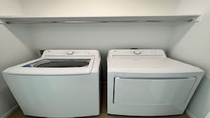 A laundry room with two front-loading washing machines and a metal shelf above them.