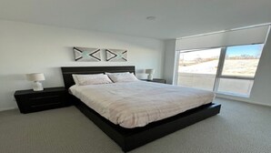 A modern bedroom with a large bed, two bedside tables, and a view of a parking lot through a large window.