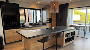 A modern kitchen with a central island, bar stools, and a large window with blinds.