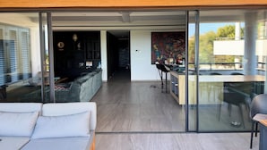 A modern interior with a glass wall, a sofa, a dining area, and a kitchen.