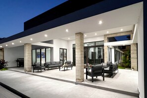An outdoor patio area with a modern design, featuring a sofa set, a dining table, and a grill.