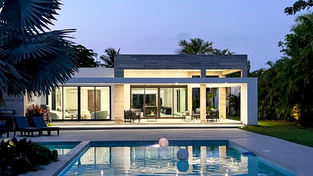 Una casa moderna con piscina, ventanas amplias y mobiliario de exterior.