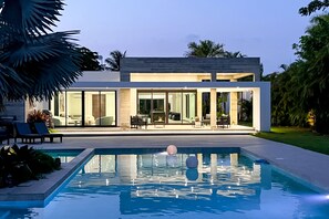 Une maison moderne dotée d’une piscine, de grandes fenêtres et de mobilier d’extérieur.