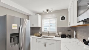 A modern kitchen with white cabinets, a stainless steel refrigerator, a sink, and a countertop with a blender and toaster. - Birmingham Retreat - Relax & Enjoy (Birmingham)