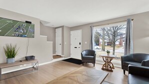 A modern living room with a large TV, comfortable seating, a wooden coffee table, and a view of the outside. - Birmingham Retreat - Relax & Enjoy (Birmingham)