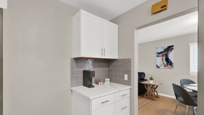 A compact kitchen with white cabinets, a coffee machine, and a small table with chairs. - Birmingham Retreat - Relax & Enjoy (Birmingham)