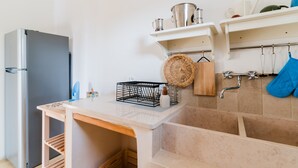 Een keuken met een koelkast, een houten tafel, een spoelbak en een rek met keukengerei.