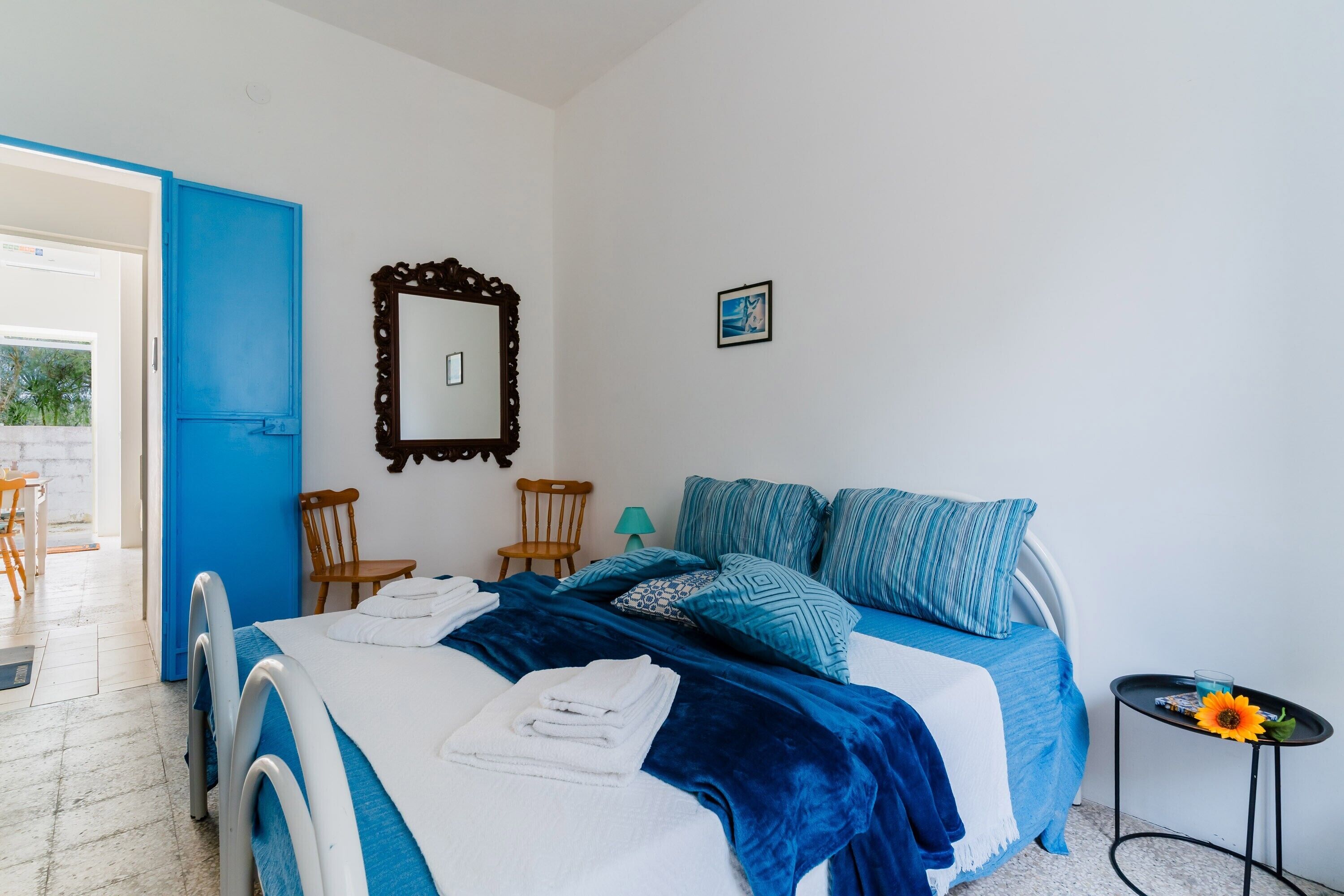 A bedroom with a bed, chairs, a table, a mirror, and a picture on the wall.