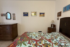 Une chambre à coucher comprenant un lit, une commode, une table de chevet, une lampe et des œuvres d’art murales.