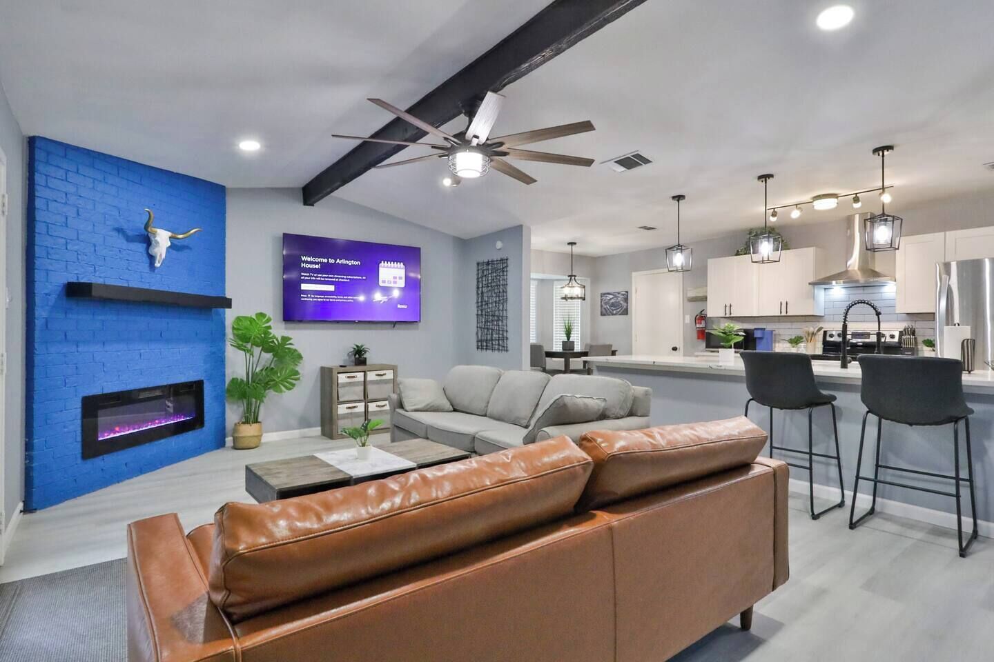 A modern living room with a blue brick wall, a fireplace, a leather sofa, and a television displaying a welcome message.