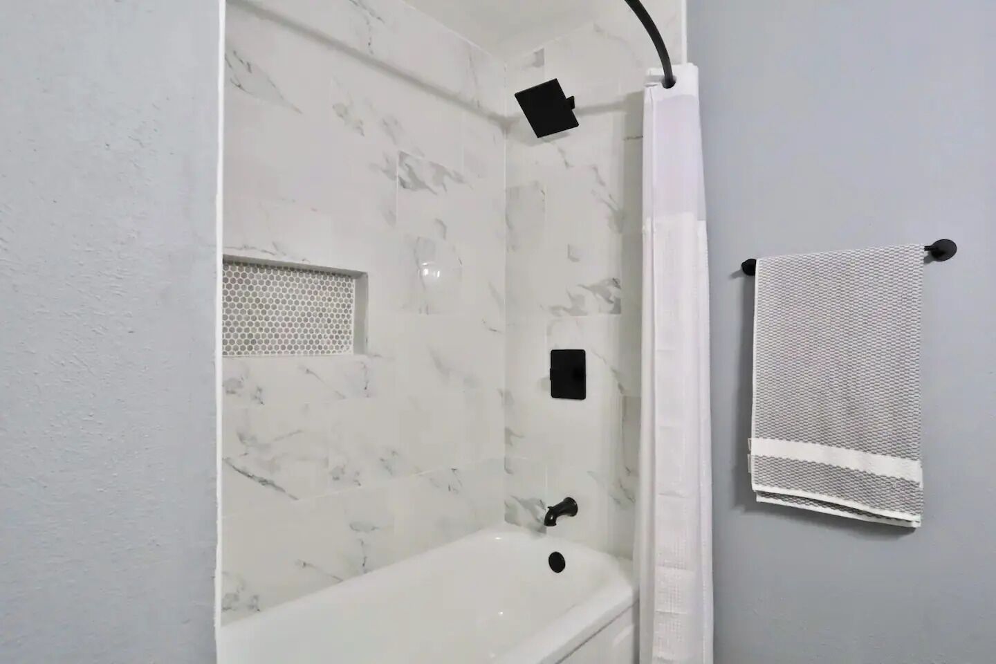 Une salle de bain avec un mur en marbre blanc, une baignoire blanche, un rideau de douche et un porte-serviettes avec une serviette.