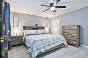 Ein Schlafzimmer mit Bett, Nachttischen, Kommode, Deckenventilator und einer Tür.
