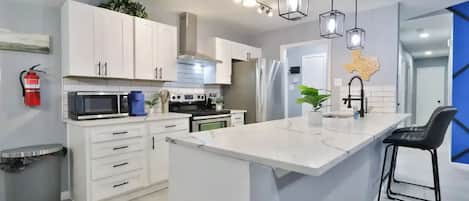 Une cuisine moderne avec des meubles blancs, un îlot central et des luminaires suspendus.