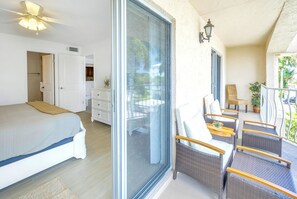 Ein Schlafzimmer mit einem großen Bett, einer Glastür zu einem Balkon, Korbmöbeln und einem Deckenventilator.