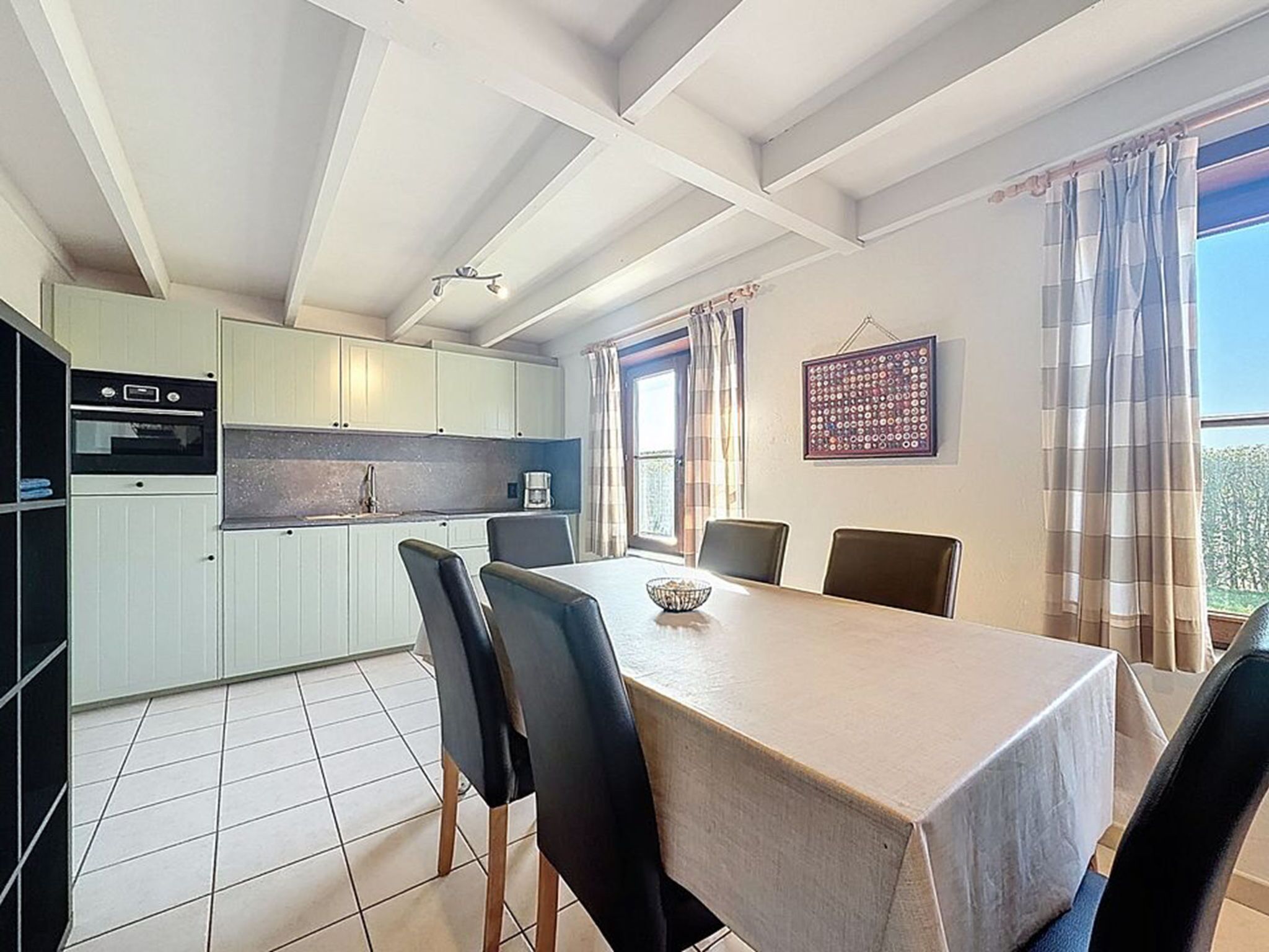 A modern kitchen with white cabinets, a dining table with chairs, and a view of the outdoors through large windows.
