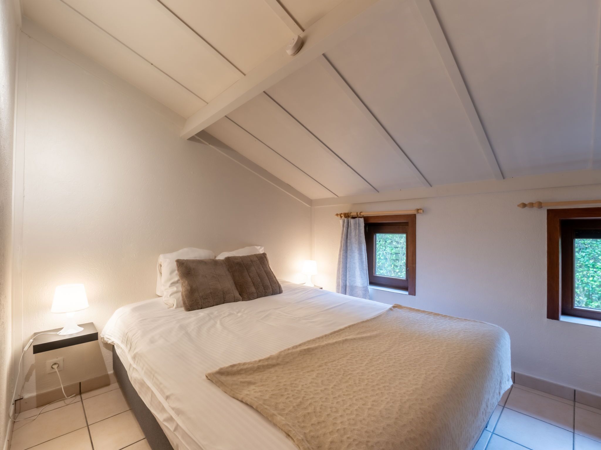 Une chambre à coucher avec un lit, une table de chevet, une lampe et des fenêtres.