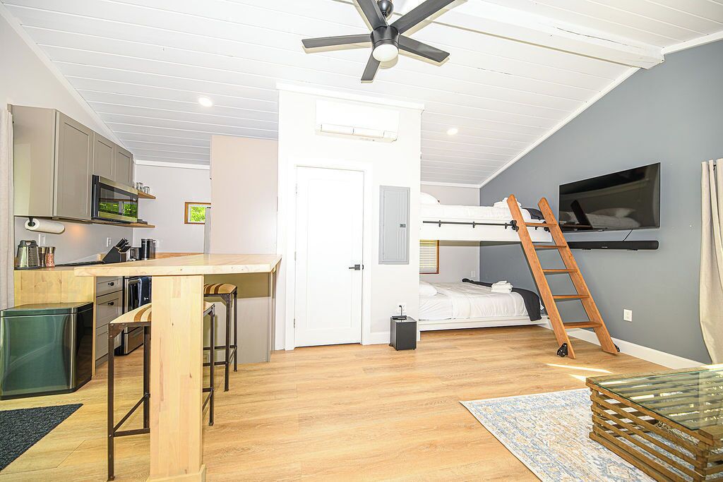 A compact room with a kitchenette, a bed, a TV, and a ladder.