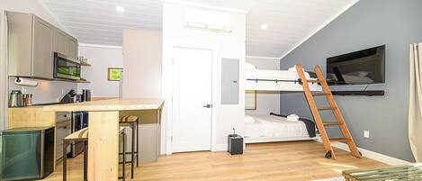 A compact room with a kitchenette, a bed, a TV, and a ladder.
