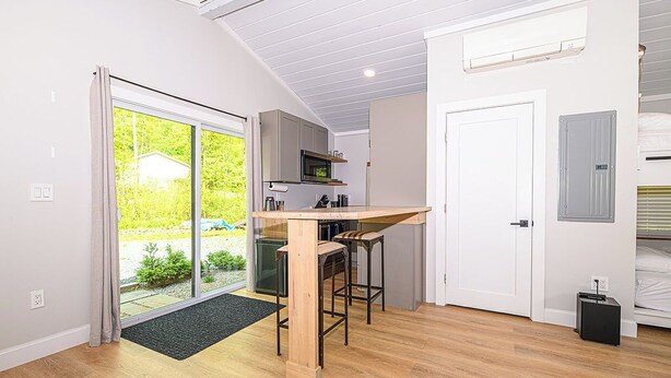 Cocina compacta con taburete de bar, puerta corrediza de vidrio que da a un jardín y una puerta blanca con un armario pequeño.
