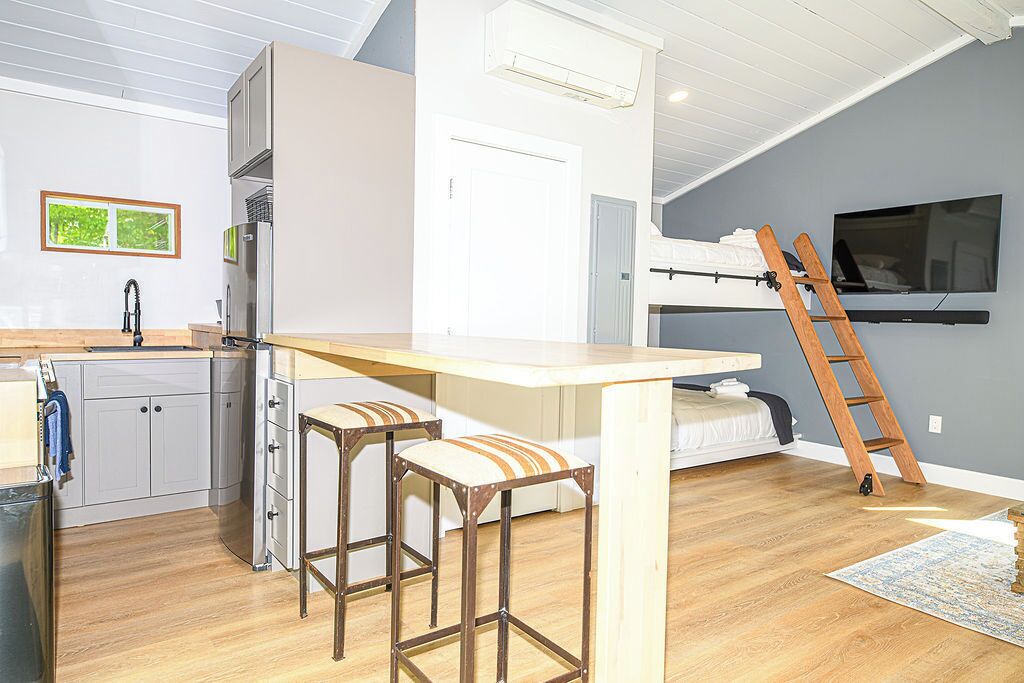 A compact kitchen with a wooden countertop, two stools, a refrigerator, and a built-in bench.