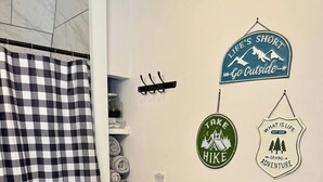 Een badkamer met een douchegordijn met ruitpatroon, een houten plankje met handdoeken en inspirerende muurstickers.