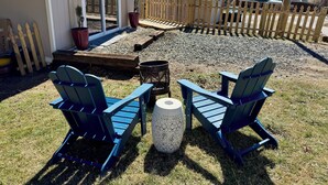 Een achtertuin met een houten terras, een vuurkuil en twee blauwe Adirondack-stoelen.