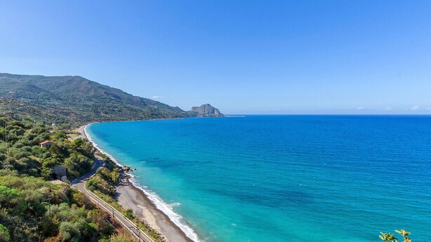 Une route côtière bordée d’une plage, avec une montagne en arrière-plan.