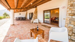 Un patio couvert avec des murs en pierre, un plafond en bois et un ensemble de mobilier de salle à manger.
