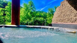 Piscina cristalina con un muro de piedra y vegetación al fondo.