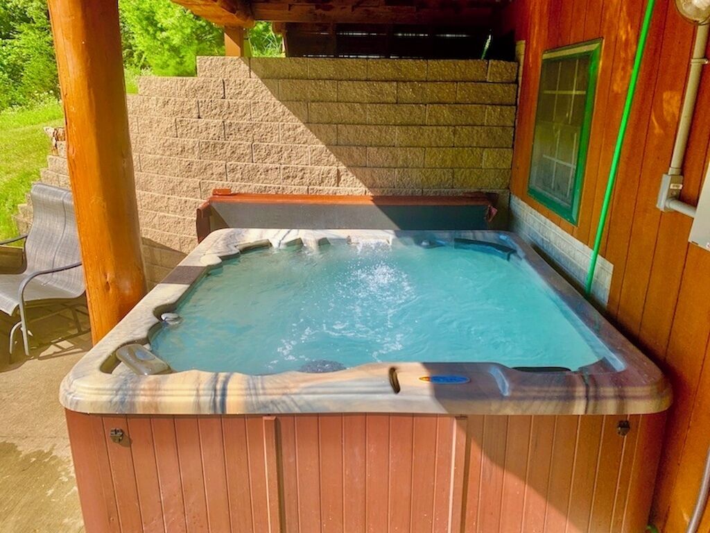 Un bain à remous avec un revêtement extérieur en bois, un mur de pierre en arrière-plan et une fenêtre donnant sur un paysage verdoyant.