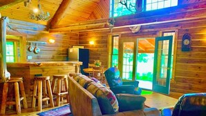 Interior acogedor de una cabaña con zona de comedor de madera, sofá y barra.