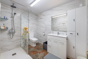 Un baño moderno con ducha de vidrio, inodoro, lavabo con espejo y armarios.