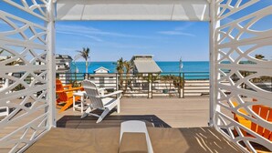 A beach view from a covered deck with a white lattice structure, a pool, and a chair. - Dolce Vita: Amazing Rooftop Experience, Views, Pool, Spa by Anna Maria Life Vacation Rentals (Anna Maria)