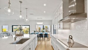 A modern kitchen with a large island, stainless steel appliances, and a view to the outdoors. - Dolce Vita: Amazing Rooftop Experience, Views, Pool, Spa by Anna Maria Life Vacation Rentals (Anna Maria)