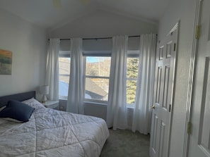 A bedroom with a bed, a nightstand, a lamp, and a window with curtains.
