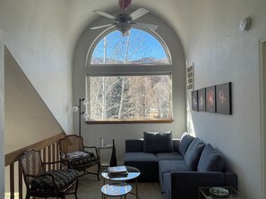 A cozy living room with a large arched window, a ceiling fan, and a sofa.