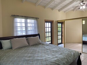 Een slaapkamer met een bed, een raam met gordijnen, een deur en een plafondventilator.