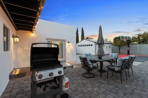 Terrassa exterior amb una barbacoa, taula i cadires, i un cèrcol de bàsquet.