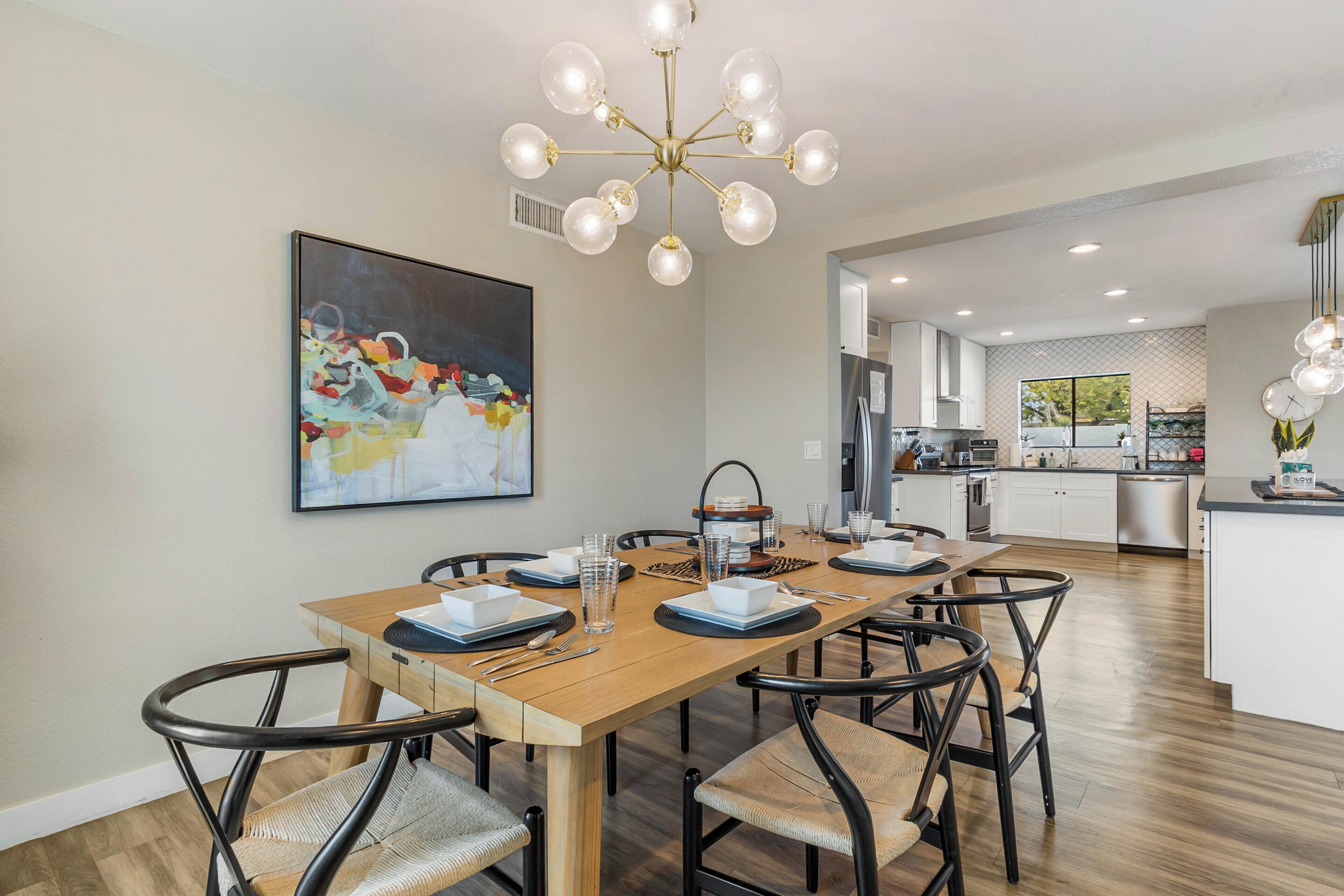 A modern kitchen with white cabinets, a wooden dining table, and a chandelier.