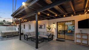 An outdoor patio area with a covered seating area, a hot tub, and a television mounted on the wall. - Scottsdale Day Dream - Spacious modern home with Private Pool, Hot Tub, and Firepit (Scottsdale)