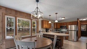Une cuisine moderne avec des meubles en bois, des appareils en acier inoxydable et de grandes fenêtres offrant une vue sur l’extérieur.