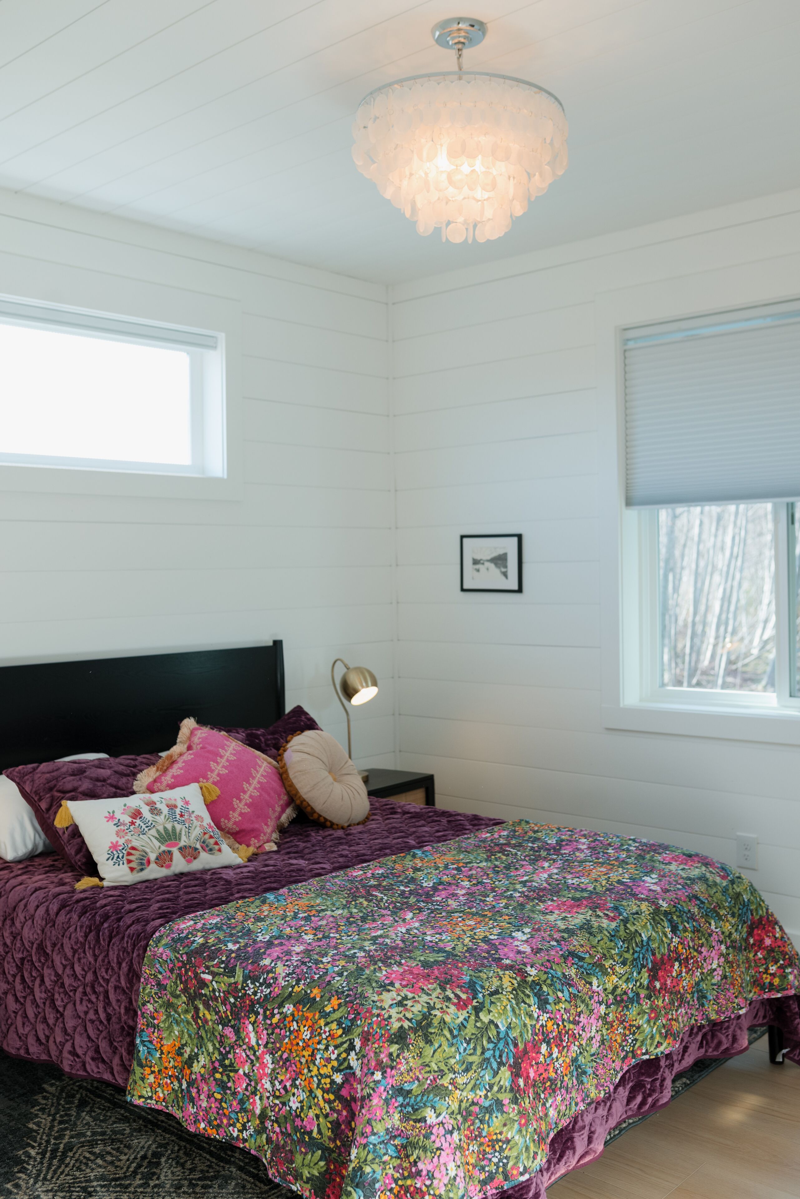 A bedroom with a bed, a chandelier, a window, and a picture on the wall.