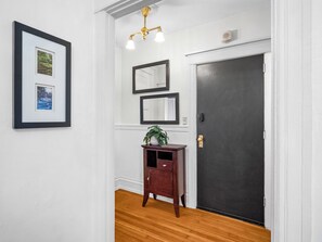 A hallway with a wooden floor, a dark door, and a small wooden cabinet with a plant.