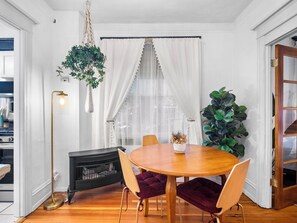 A dining area with a round wooden table, two chairs, a hanging plant, and a black wood-burning stove.