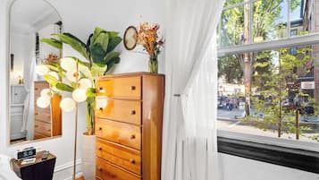 A room with a wooden dresser, a mirror, a clock, and a window with a view of the street.