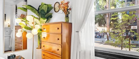 A room with a wooden dresser, a mirror, a clock, and a window with a view of the street.