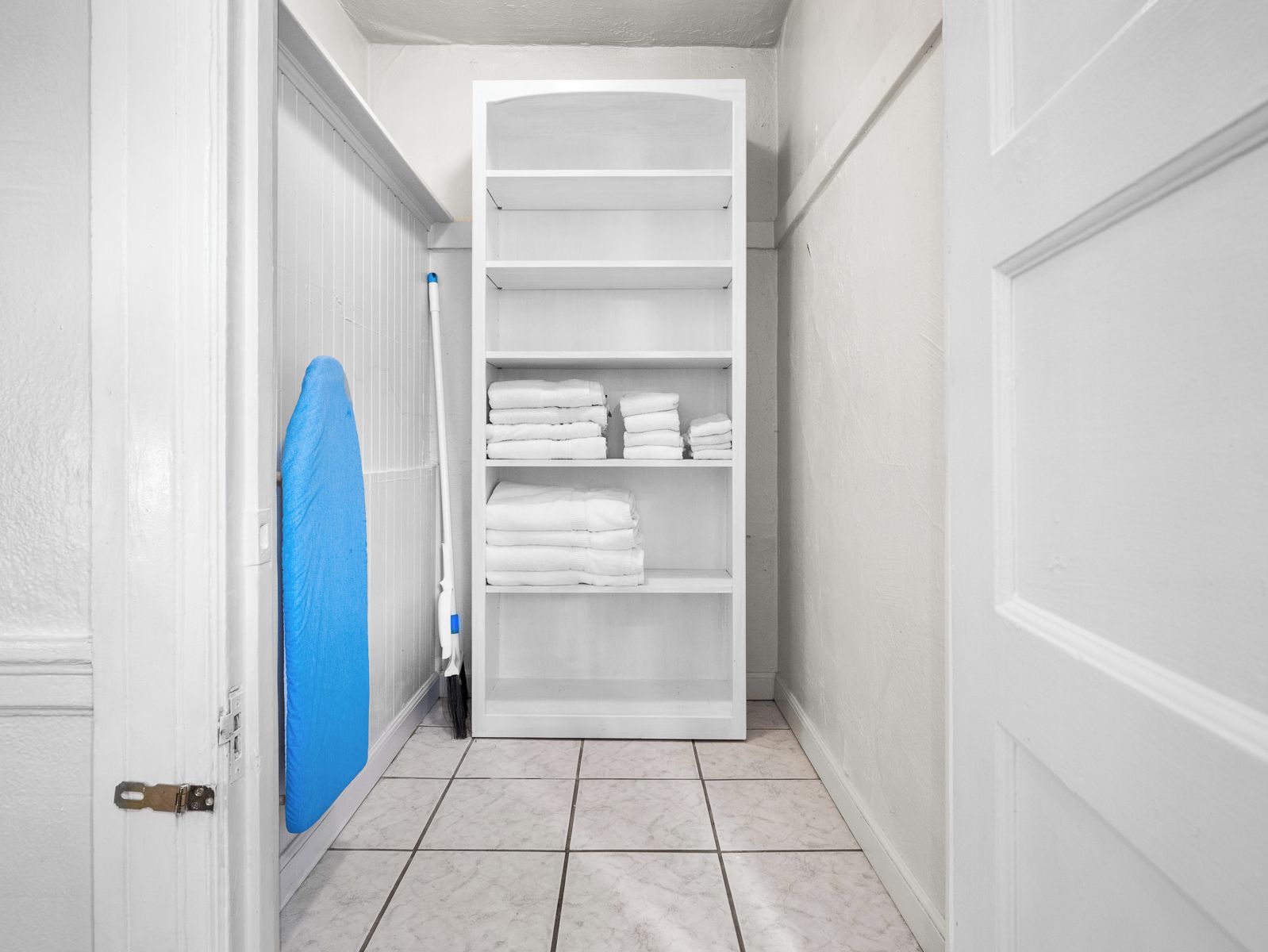 Un couloir avec une porte blanche, une serviette bleue accrochée au mur et une armoire blanche avec des étagères.