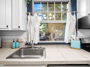Een keuken met een spoelbak van roestvrij staal, een raam met gordijnen en uitzicht op de straat.