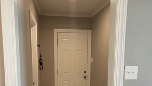 Un couloir avec un plancher en bois, une porte blanche et un petit banc en bois.
